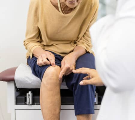 Woman sitting in patient room showing doctor where her knee hurts