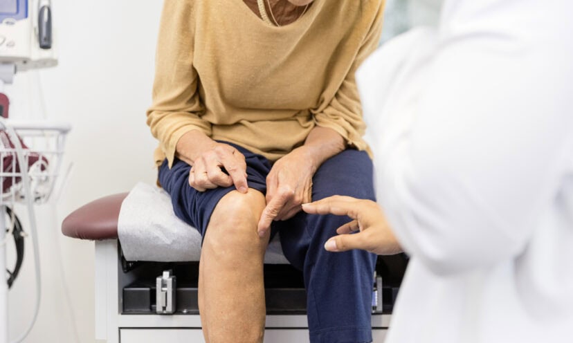 Woman sitting in patient room showing doctor where her knee hurts