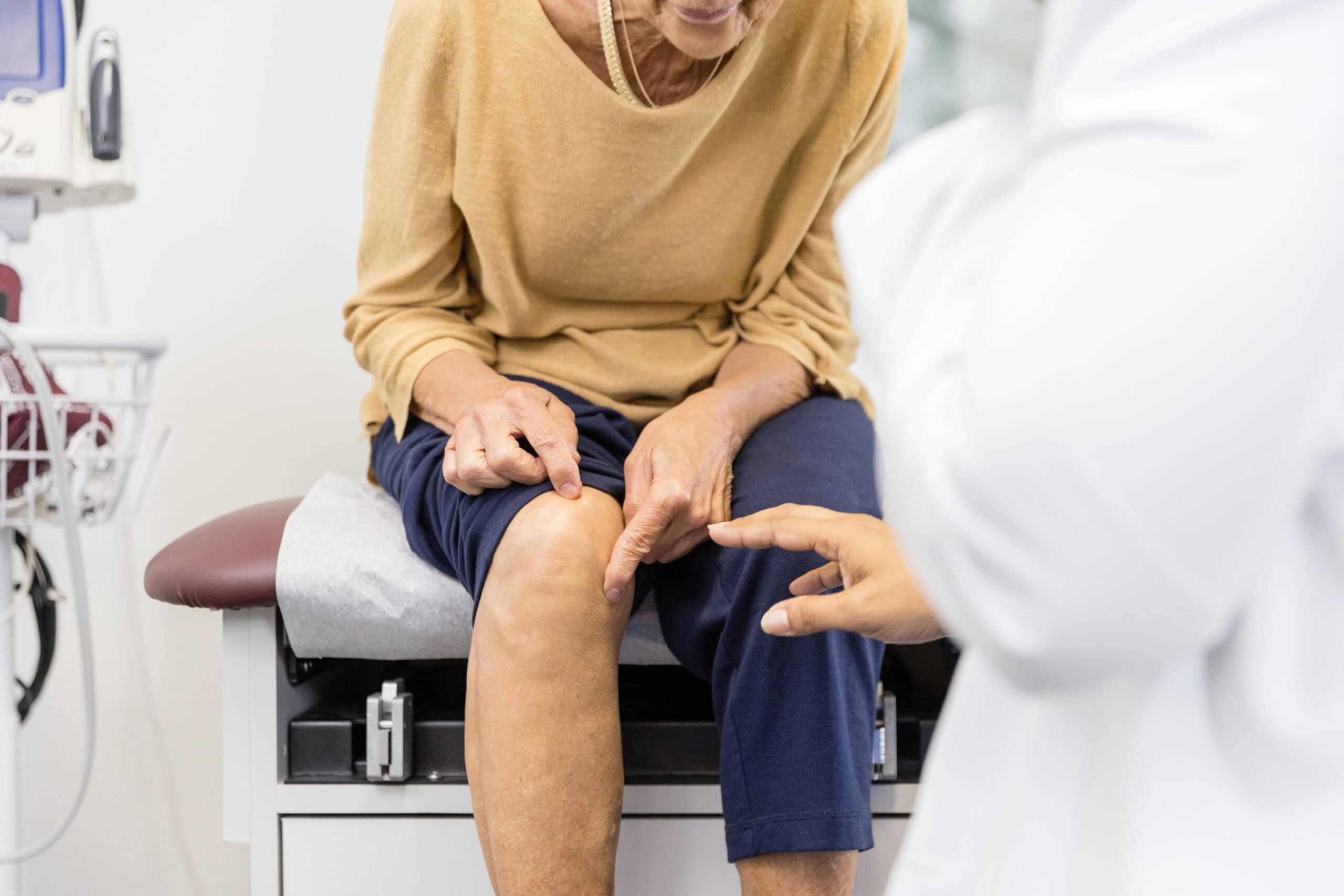Woman sitting in patient room showing doctor where her knee hurts