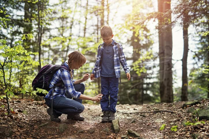 Mother and son hiking in forest. Mother is applying tick repellent on the son's legs.