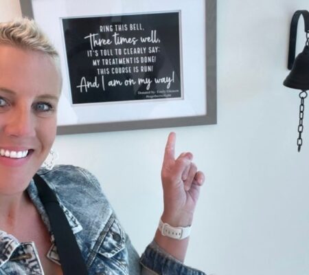 Emily Gleason, breast cancer survivor, points to bell in cancer center