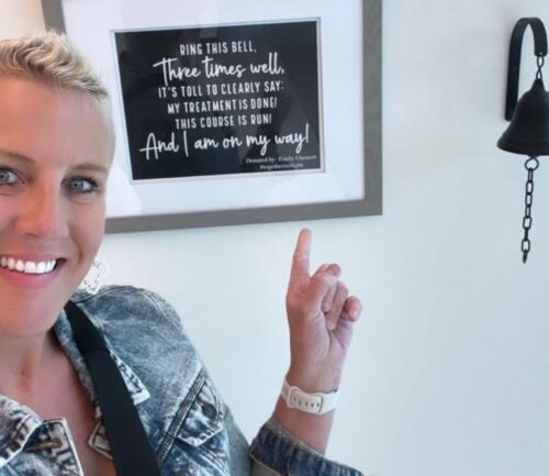 Emily Gleason, breast cancer survivor, points to bell in cancer center
