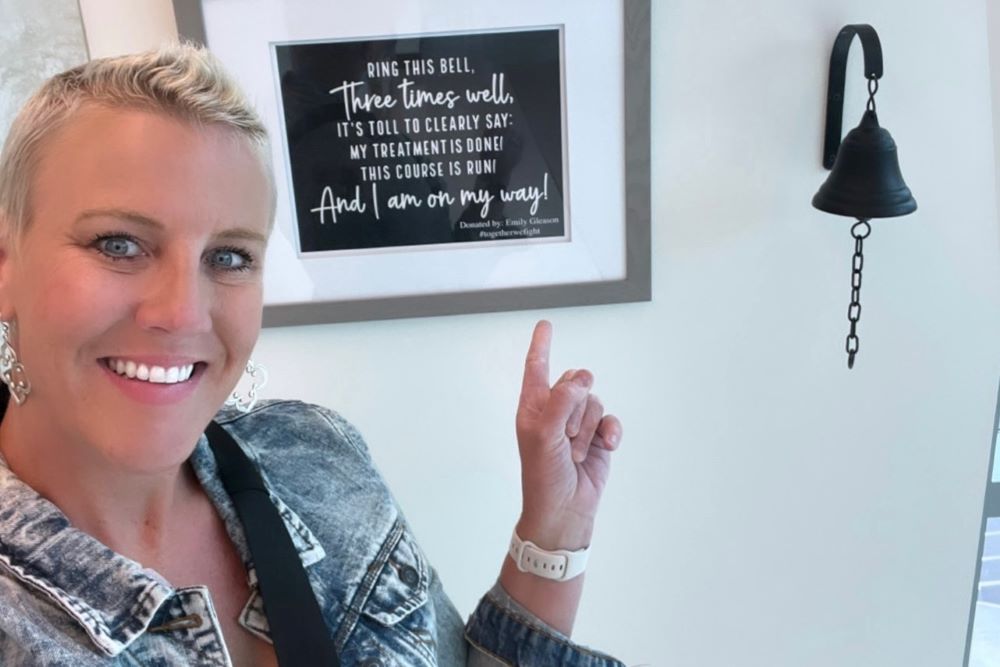 Emily Gleason, breast cancer survivor, points to bell in cancer center