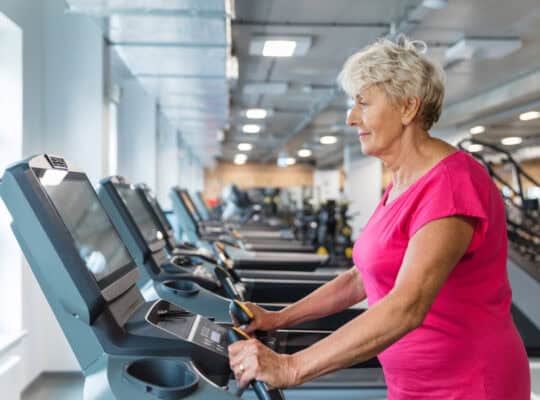 Elderly woman working out on treadmill at gym.