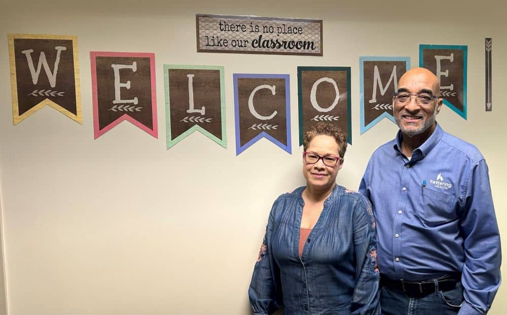 Ron and Krista Mainess pose in front of a welcome sign
