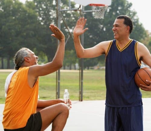 Two men high-fiving at a basketball court outside