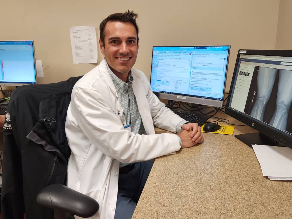Dr. Blake Daney smiling at camera in front of computer