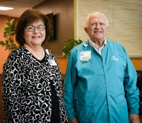 Susan Riegel and Chuck the volunteer stand at the front desk of Kettering Health Miamisburg, greeting guests.