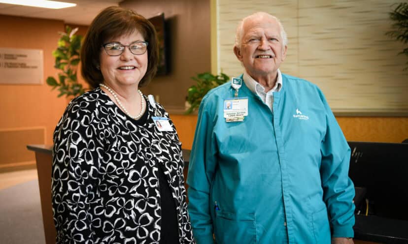Susan Riegel and Chuck the volunteer stand at the front desk of Kettering Health Miamisburg, greeting guests.