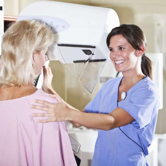 Woman in her 50s, with nurse or technician, getting a mammogram.
