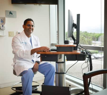 Dr. Patel sitting at a computer in front of a window