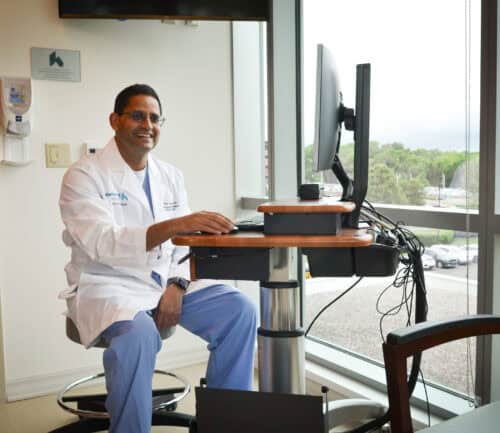 Dr. Patel sitting at a computer in front of a window