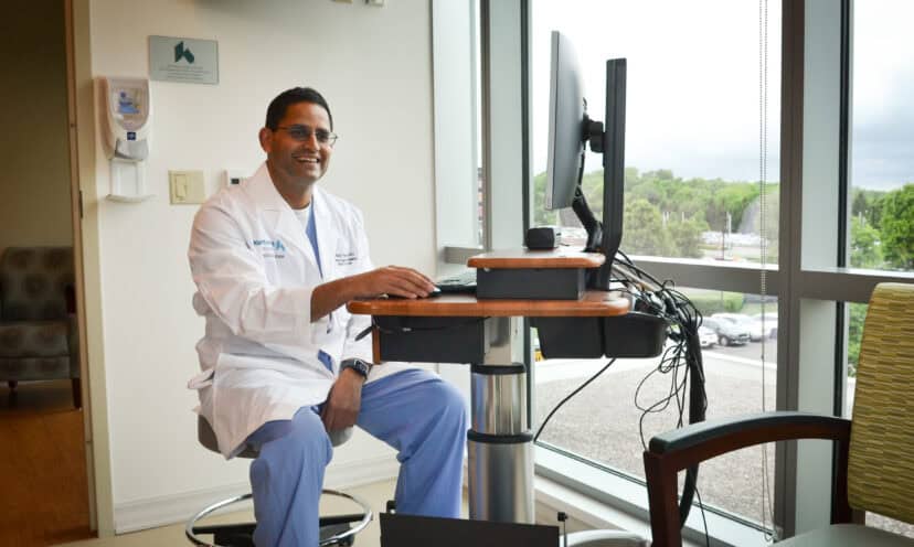 Dr. Patel sitting at a computer in front of a window