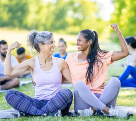 older woman and younger woman sitting outside, flexing their biceps