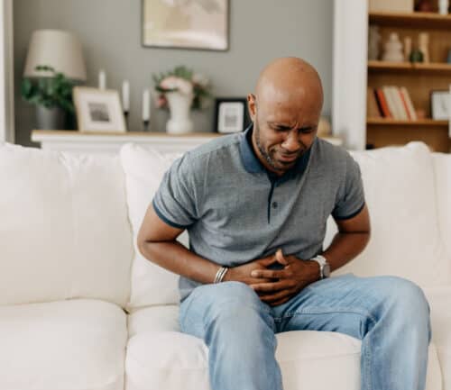 Man suffering from stomach pain on white couch indoors