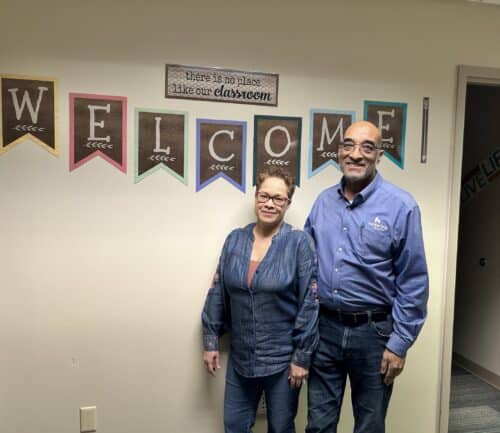 Two healthcare professionals standing together in classroom with welcome banner overhead