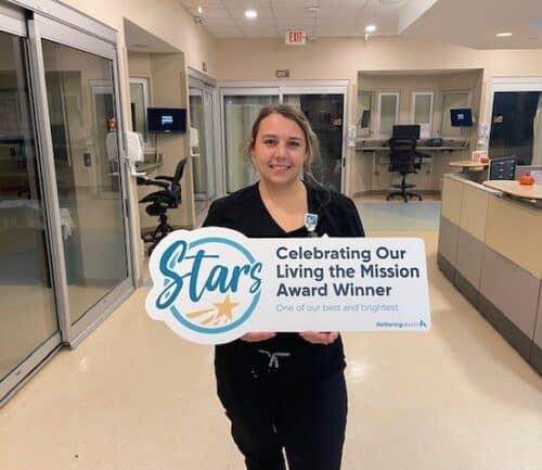 Katie Carroll stands holding a "Living the Mission" sign