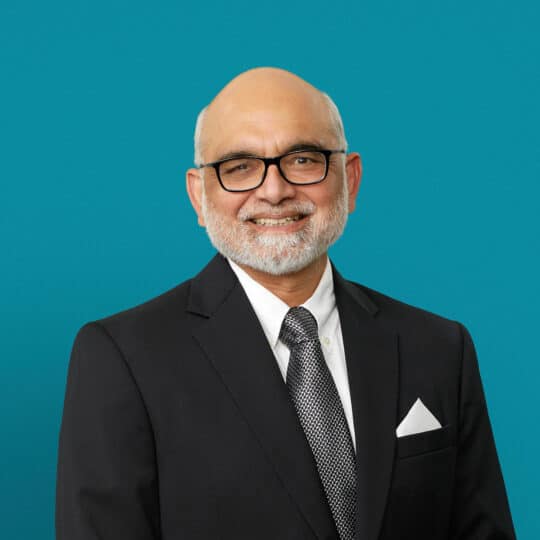 Professional headshot of Dr. Aamir Khan in dark suit against teal background