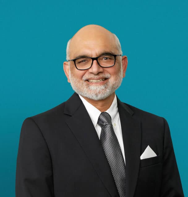 Professional headshot of Dr. Aamir Khan in dark suit against teal background