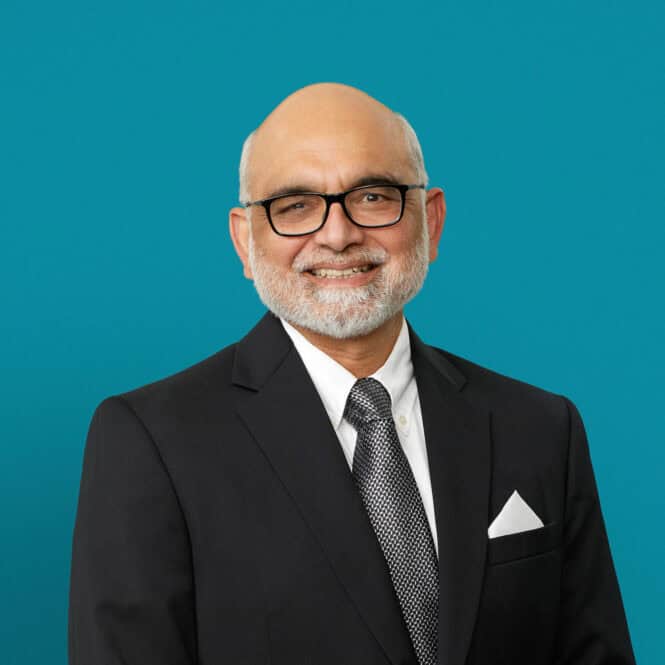 Professional headshot of Dr. Aamir Khan in dark suit against teal background