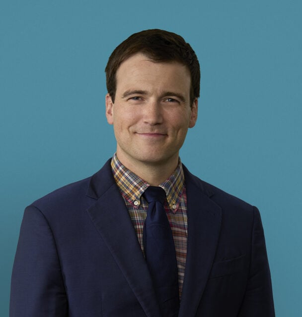 Professional headshot of Aaron Burket, DO in navy suit with plaid shirt