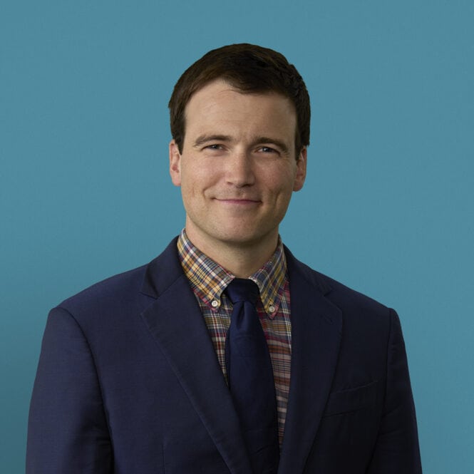 Professional headshot of Aaron Burket, DO in navy suit with plaid shirt