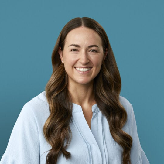 Professional headshot of Dr. Abby Hinkel smiling in white blouse against blue background