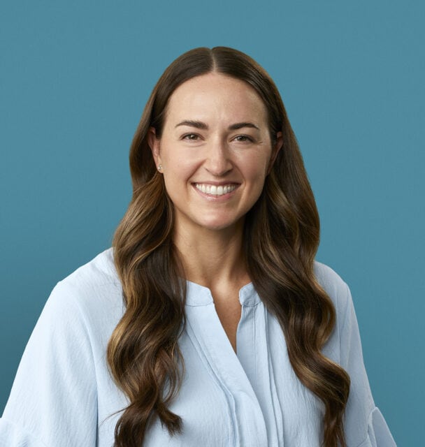 Professional headshot of Dr. Abby Hinkel smiling in white blouse against blue background