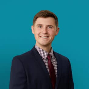 Professional headshot of Abram Basinger, APRN-CNP in navy suit with burgundy tie