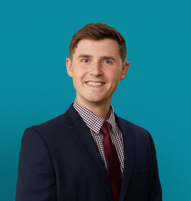 Professional headshot of Abram Basinger, APRN-CNP in navy suit with burgundy tie