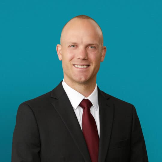 Professional headshot of Adam Bussey, MD in dark suit with red tie