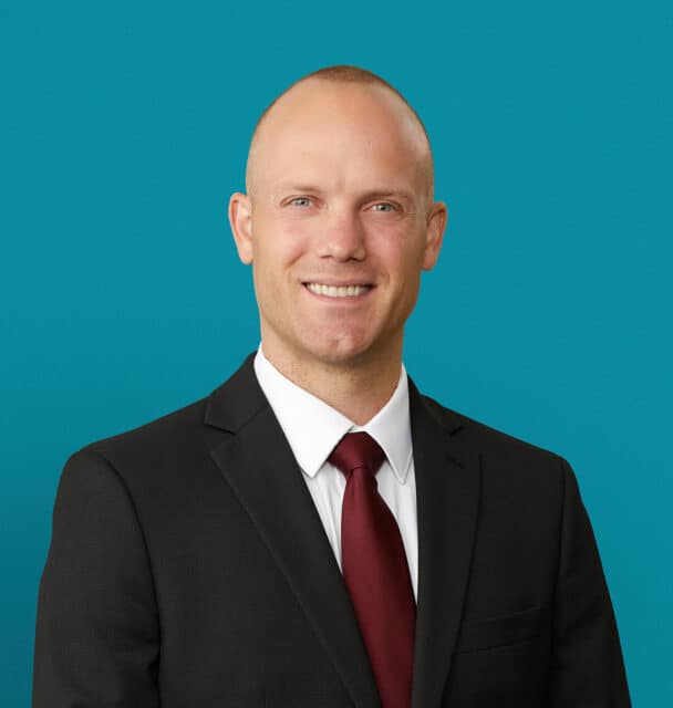 Professional headshot of Adam Bussey, MD in dark suit with red tie