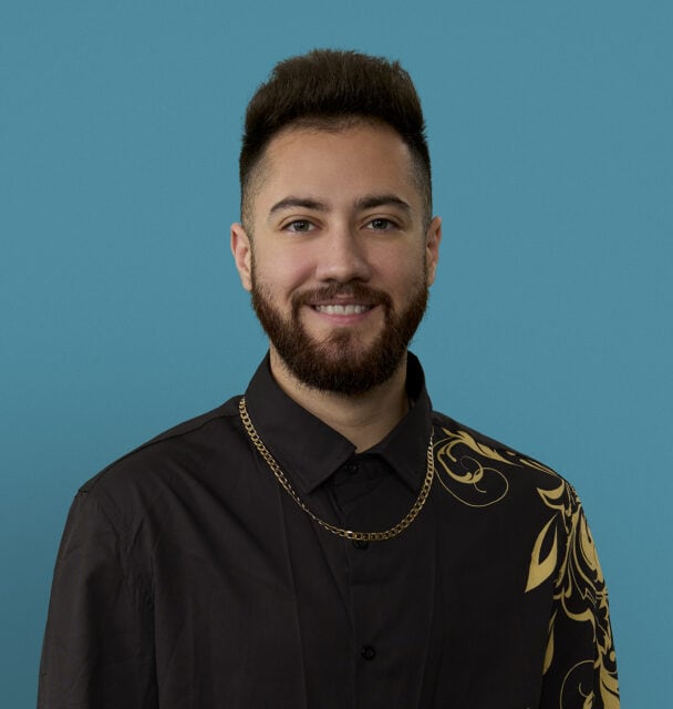 Professional headshot of Dr. Aelius Khan smiling in black shirt with gold chain