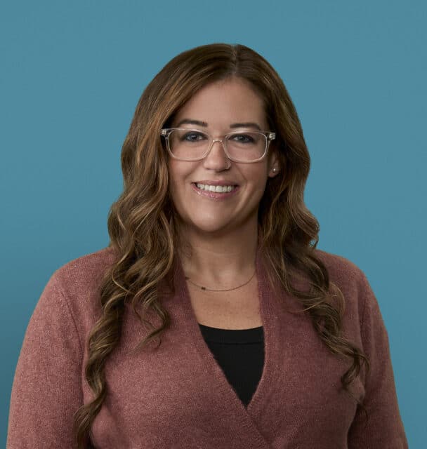 Professional headshot of Alyson Spiller, APRN-CNP, smiling in burgundy cardigan against blue background