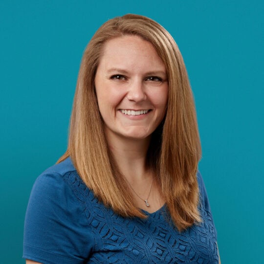 Professional headshot of Andrea Jez, PA-C, smiling in blue top against teal background
