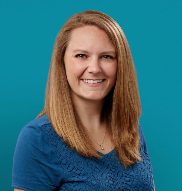 Professional headshot of Andrea Jez, PA-C, smiling in blue top against teal background