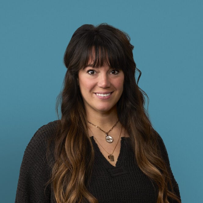 Professional headshot of Andrea Smith, APRN-CNP, smiling in dark sweater against blue background