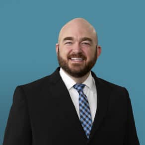 Professional headshot of Andrew Costerisan, PA-C in dark suit with blue checkered tie