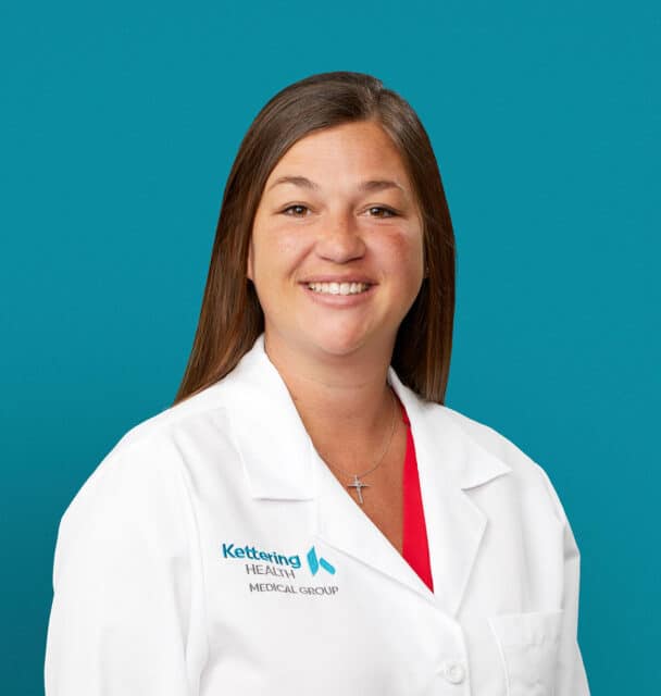 Professional headshot of Ashley Thompson, APRN-CNP in white medical coat against teal background