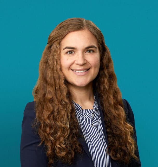 Professional headshot of Dr. Audrey Grenga in navy blazer against teal background
