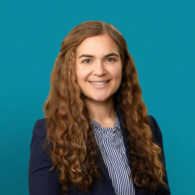 Professional headshot of Dr. Audrey Grenga in navy blazer against teal background