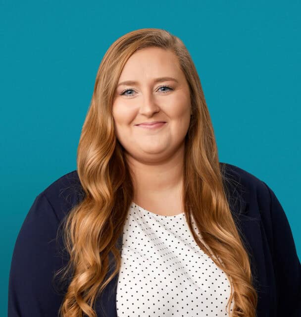 Professional headshot of Caroline Symons, PA-C against teal background wearing navy blazer