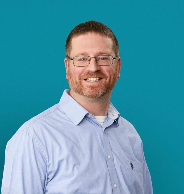 Professional headshot of Charles J. Uhl, APRN-CNP, smiling in light blue shirt against teal background