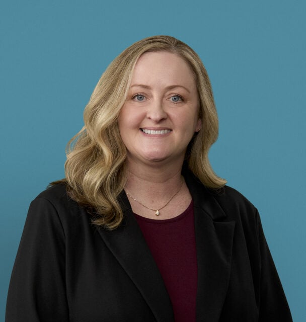 Professional headshot of Christie Astor, APRN-CNP, smiling in dark blazer against blue background