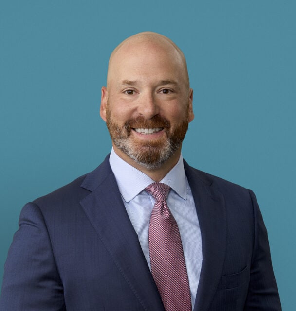 Professional headshot of Christopher J. Strauchon, DO in navy suit against teal background