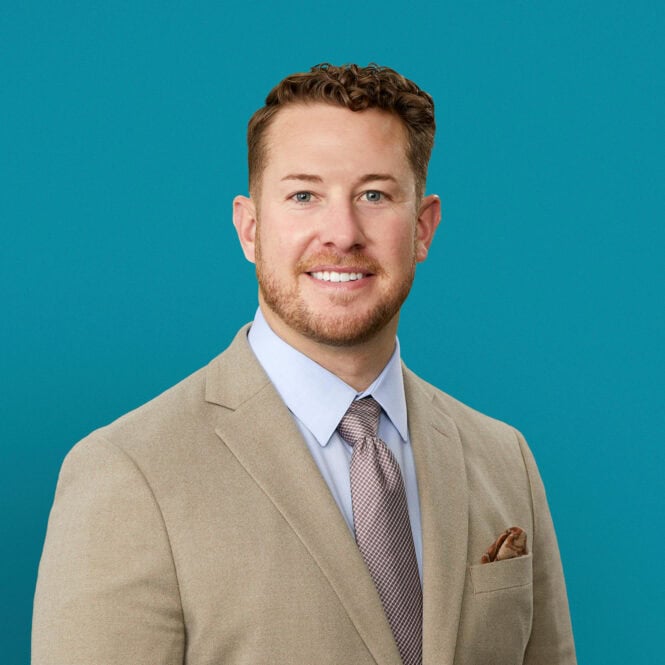 Professional headshot of Dr. Cord Gothard in tan suit against teal background