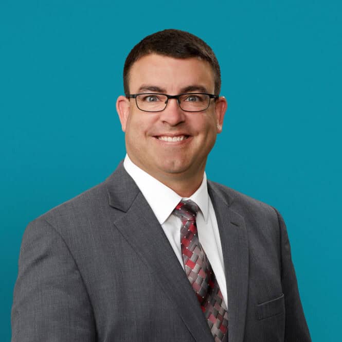 Professional headshot of Dale Guinther, APRN-CNP in gray suit with glasses smiling
