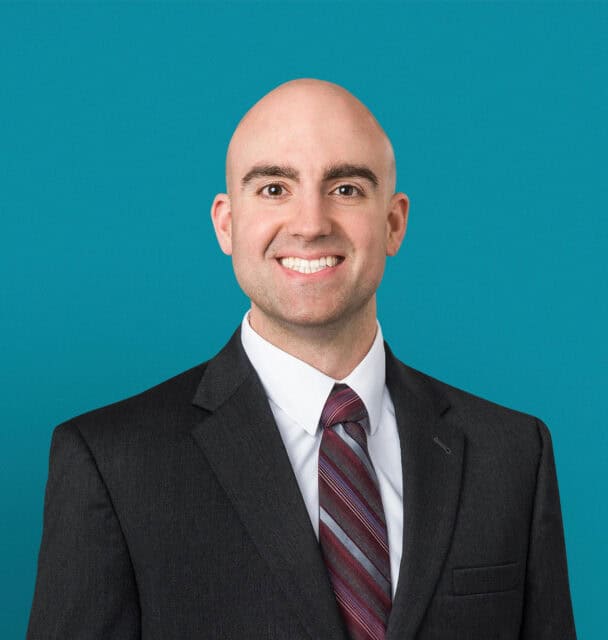 Professional headshot of Daniel Dekoski, DO in dark suit against teal background