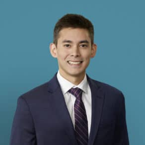 Professional headshot of Daniel Manzanillo, DO in navy suit against blue background