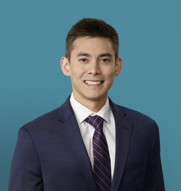 Professional headshot of Daniel Manzanillo, DO in navy suit against blue background
